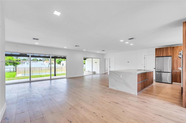 kitchen with stainless steel refrigerator, light stone countertops, a center island, and light hardwood / wood-style floors