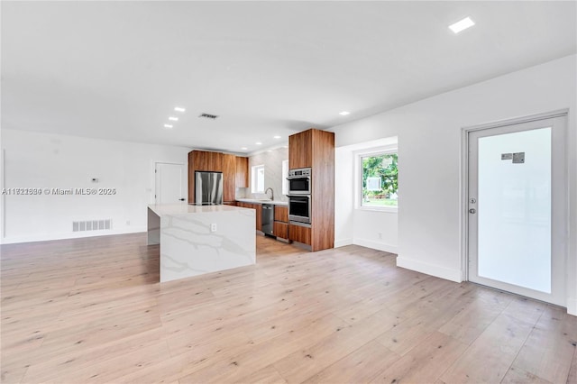 kitchen featuring sink, light hardwood / wood-style flooring, appliances with stainless steel finishes, a kitchen island, and light stone counters