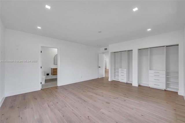 unfurnished bedroom with multiple closets, light wood-type flooring, and ensuite bath