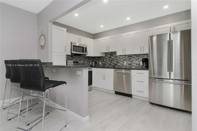 kitchen featuring kitchen peninsula, a breakfast bar, white cabinets, and appliances with stainless steel finishes