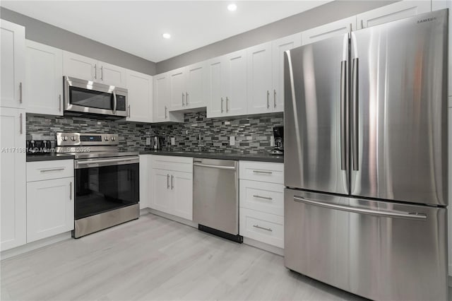 kitchen with backsplash, white cabinets, stainless steel appliances, and light hardwood / wood-style floors