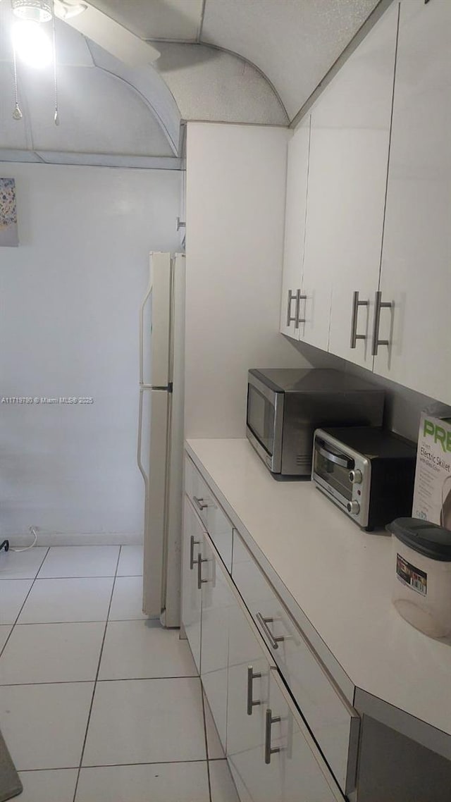 kitchen featuring white refrigerator, light tile patterned flooring, and white cabinetry