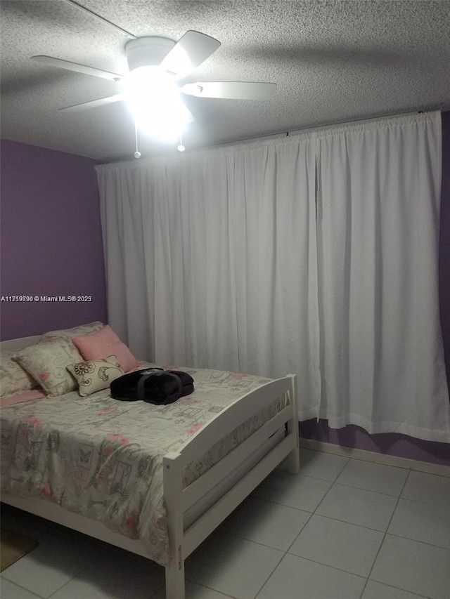 bedroom featuring ceiling fan, light tile patterned floors, and a textured ceiling