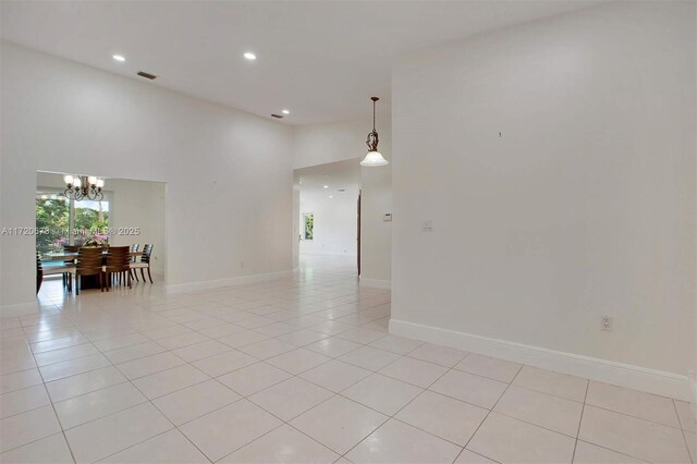 tiled empty room featuring a chandelier and a high ceiling