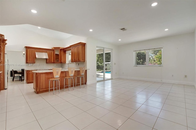 kitchen featuring ventilation hood, kitchen peninsula, vaulted ceiling, a kitchen bar, and light tile patterned floors