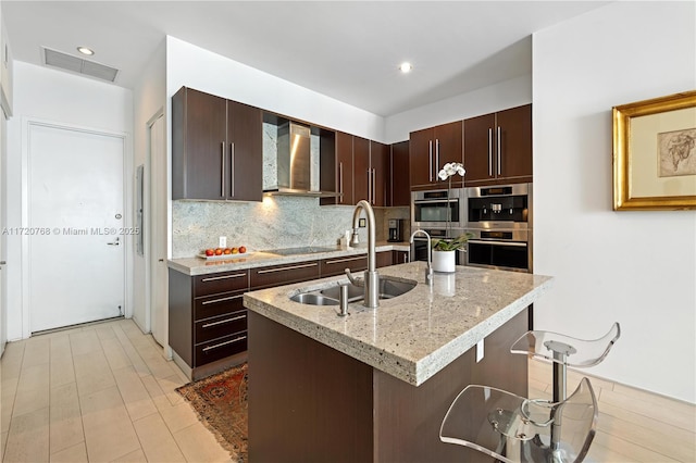 kitchen featuring black electric stovetop, dark brown cabinets, sink, a kitchen island with sink, and wall chimney exhaust hood