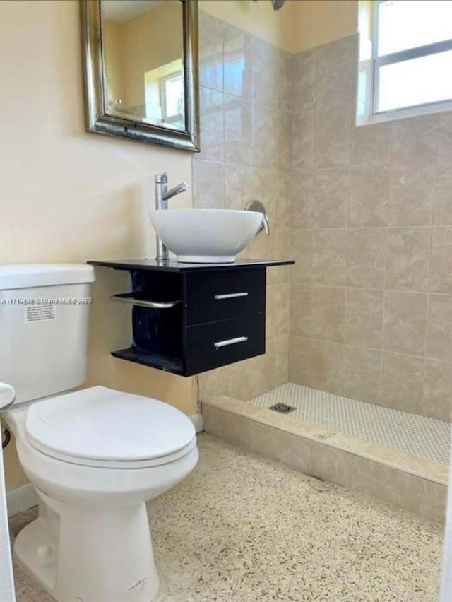 bathroom with a tile shower, vanity, and toilet