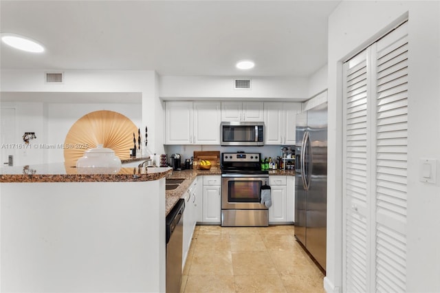 kitchen featuring kitchen peninsula, appliances with stainless steel finishes, dark stone countertops, white cabinets, and sink