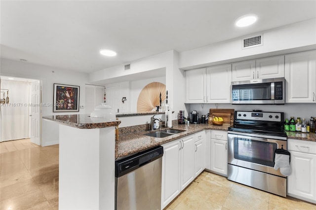 kitchen with white cabinets, appliances with stainless steel finishes, dark stone counters, sink, and kitchen peninsula