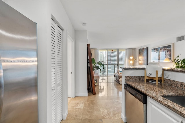 kitchen with a wall of windows, dark stone countertops, dishwasher, white cabinets, and sink