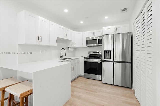 kitchen with white cabinets, light wood-type flooring, stainless steel appliances, and sink