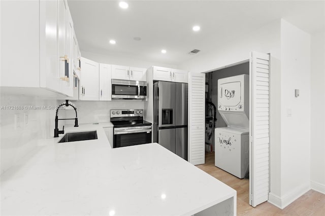 kitchen featuring sink, stainless steel appliances, stacked washer / drying machine, white cabinets, and light wood-type flooring