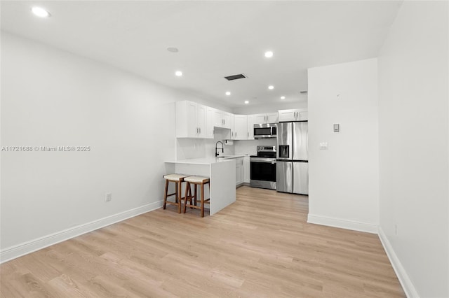 kitchen featuring white cabinetry, stainless steel appliances, kitchen peninsula, a breakfast bar, and light wood-type flooring