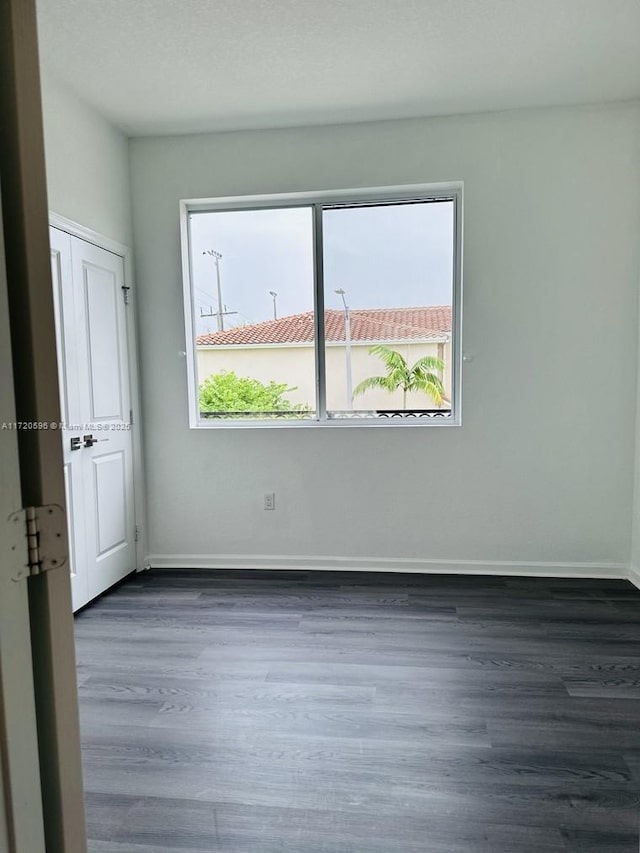 spare room featuring a healthy amount of sunlight, baseboards, and dark wood finished floors