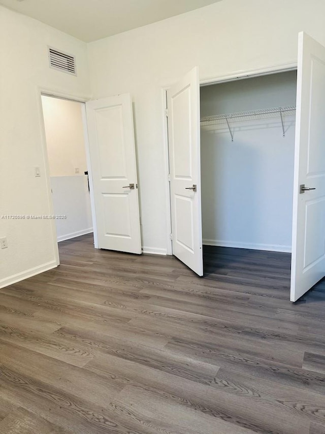 unfurnished bedroom with a closet, wood finished floors, visible vents, and baseboards