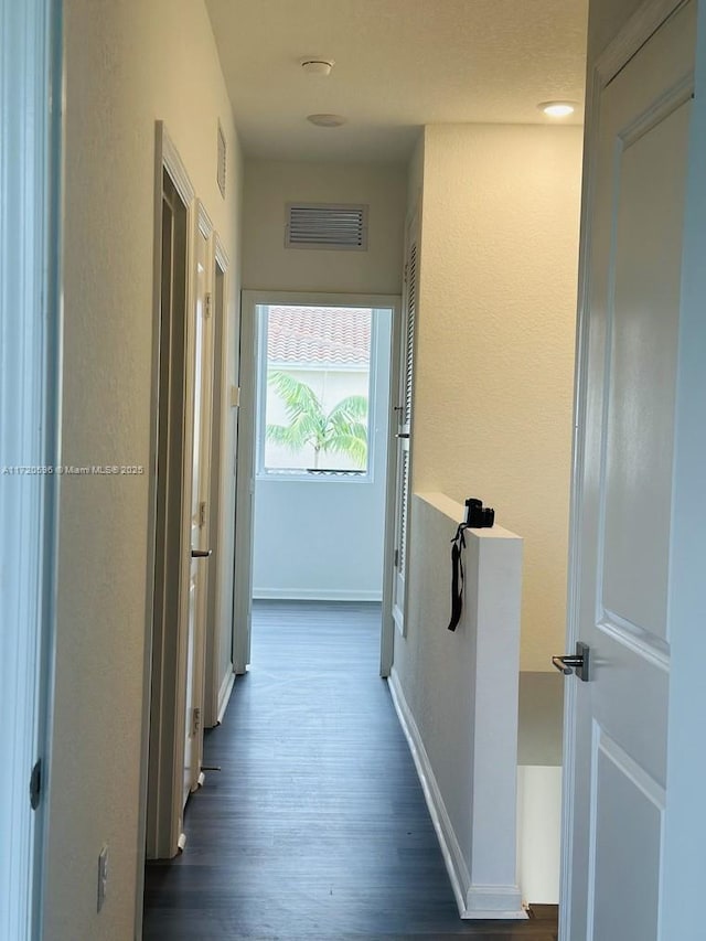 hallway with baseboards, visible vents, and dark wood-style flooring