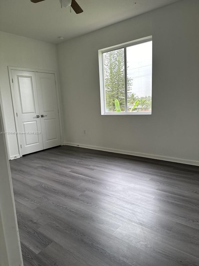 unfurnished bedroom with a closet, dark wood-style flooring, ceiling fan, and baseboards