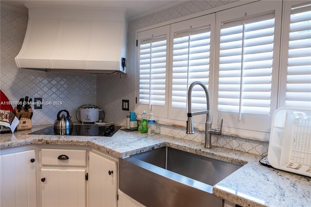 kitchen featuring decorative backsplash, black electric cooktop, extractor fan, sink, and white cabinets