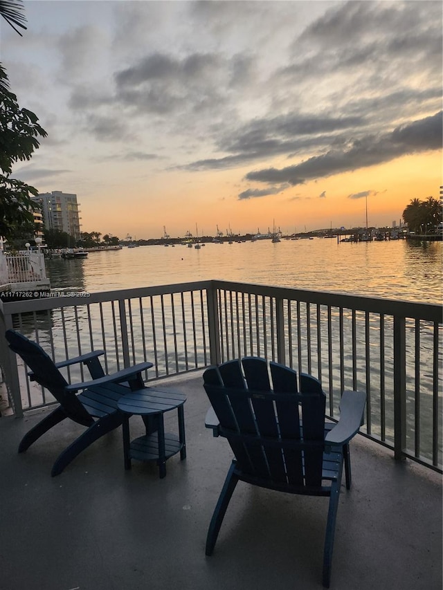 balcony at dusk featuring a water view