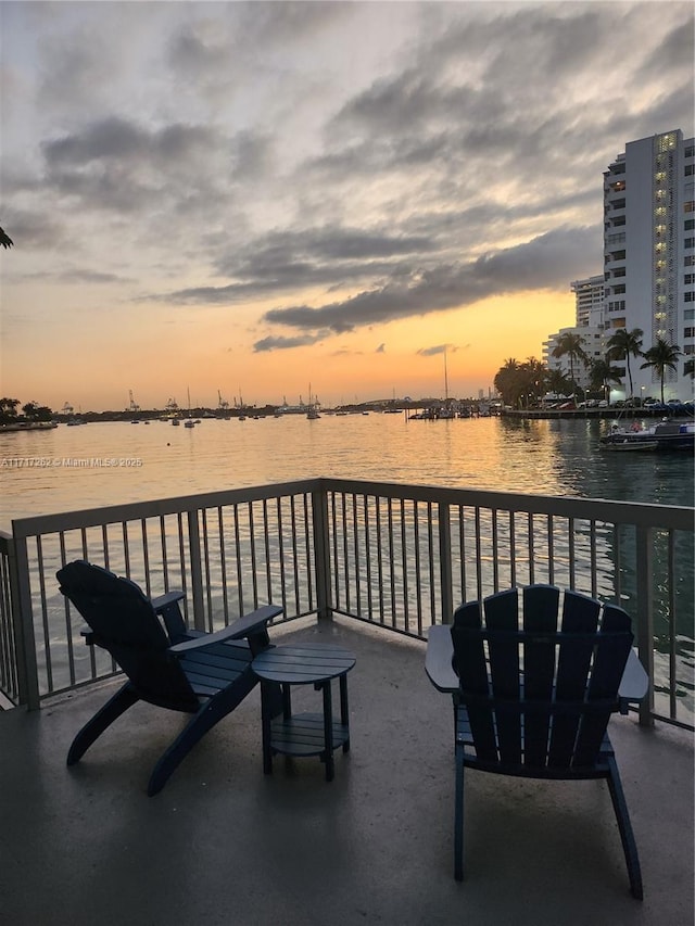 patio terrace at dusk featuring a balcony and a water view