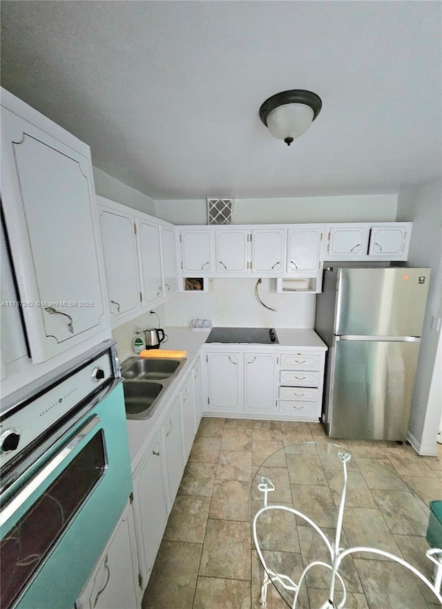 kitchen with black electric stovetop, sink, wall oven, white cabinetry, and stainless steel refrigerator