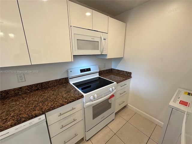 kitchen with white cabinets, light tile patterned floors, white appliances, and dark stone countertops