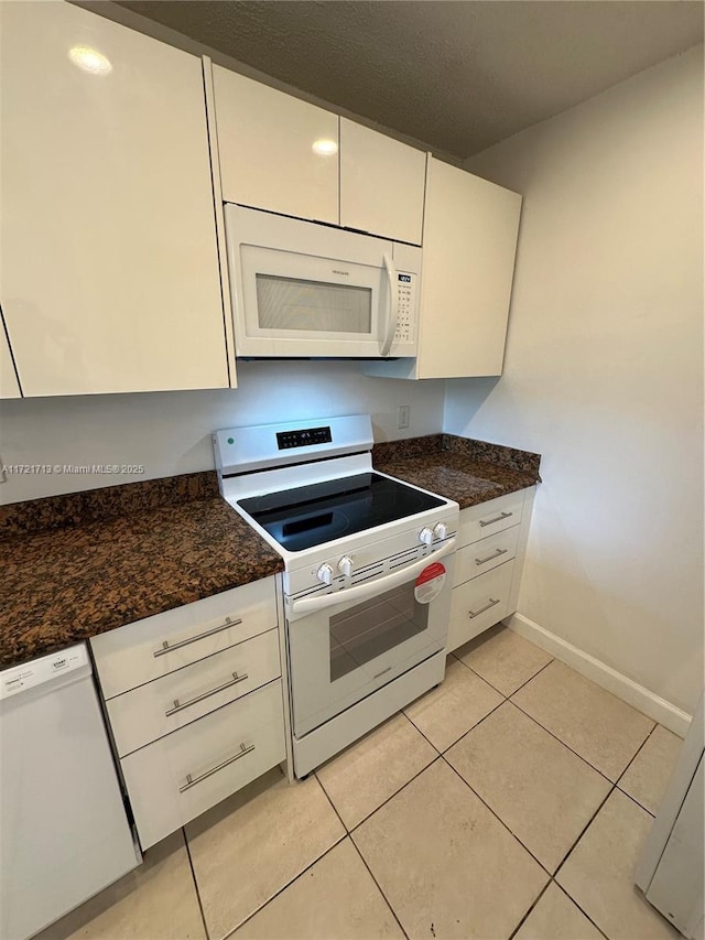 kitchen featuring light tile patterned floors, white cabinets, dark stone counters, and white appliances