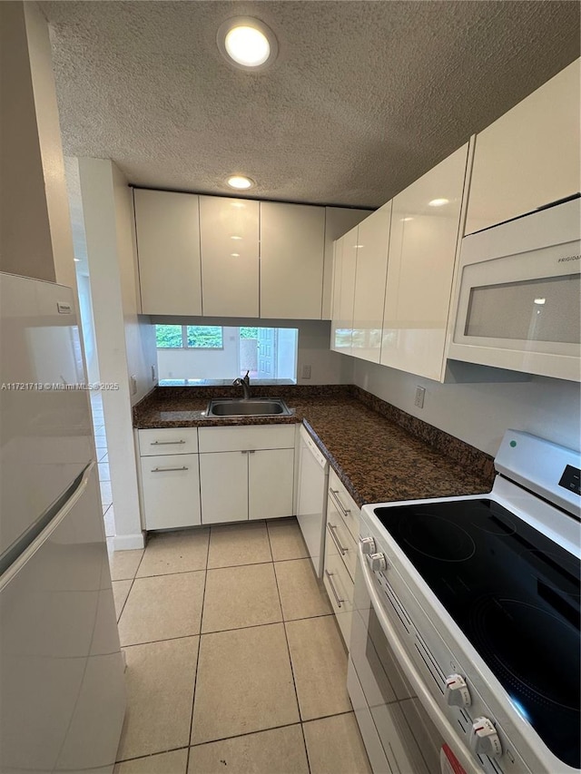 kitchen featuring dark stone counters, white appliances, sink, light tile patterned floors, and white cabinets