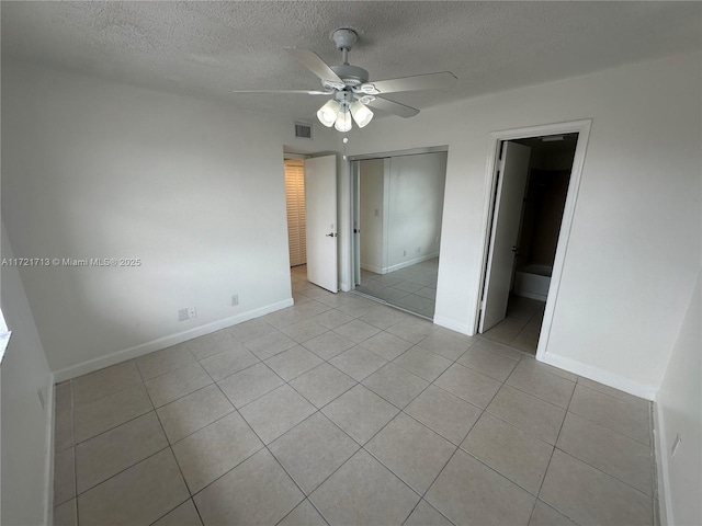 unfurnished bedroom featuring connected bathroom, ceiling fan, a textured ceiling, a closet, and light tile patterned flooring