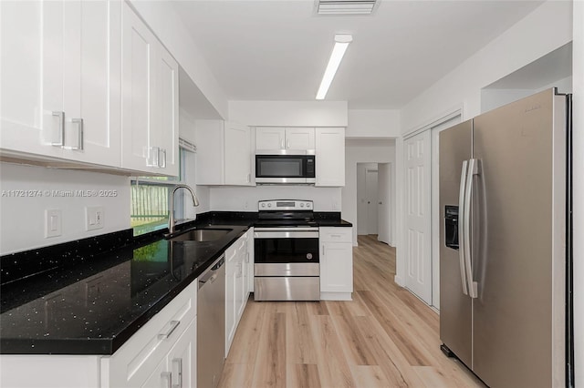 kitchen with light wood-type flooring, stainless steel appliances, sink, dark stone countertops, and white cabinetry