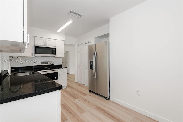 kitchen with dark stone counters, sink, light wood-type flooring, appliances with stainless steel finishes, and white cabinetry