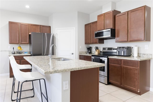 kitchen featuring a kitchen breakfast bar, stainless steel appliances, sink, light tile patterned floors, and a center island with sink