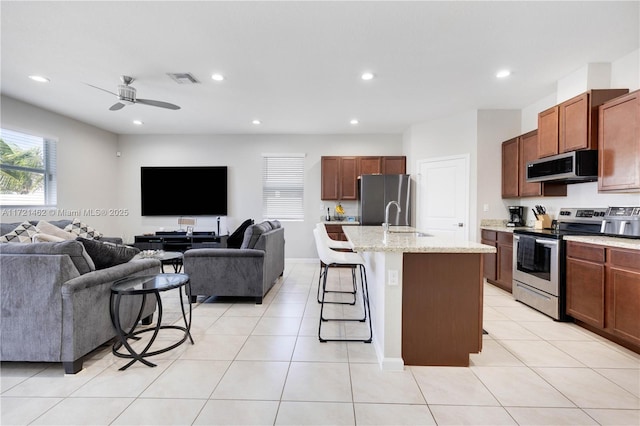 kitchen with a kitchen bar, appliances with stainless steel finishes, ceiling fan, light tile patterned floors, and an island with sink