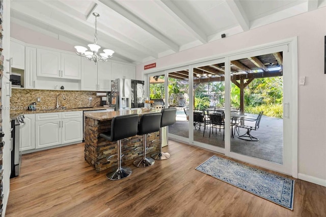 kitchen featuring light stone counters, decorative backsplash, vaulted ceiling with beams, white cabinets, and stainless steel refrigerator with ice dispenser