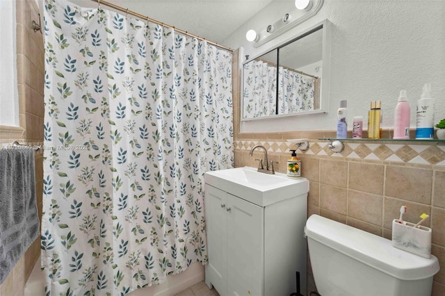 bathroom with wainscoting, toilet, vanity, and tile walls