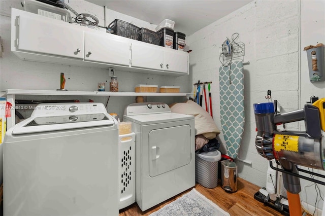 washroom featuring washing machine and dryer, wood finished floors, and cabinet space