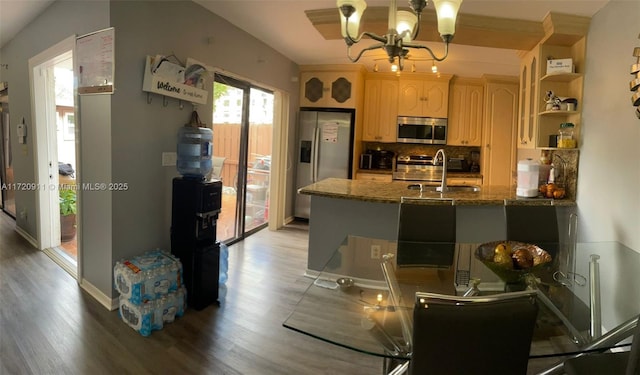 kitchen featuring light brown cabinetry, stainless steel appliances, wood-type flooring, a notable chandelier, and stone counters