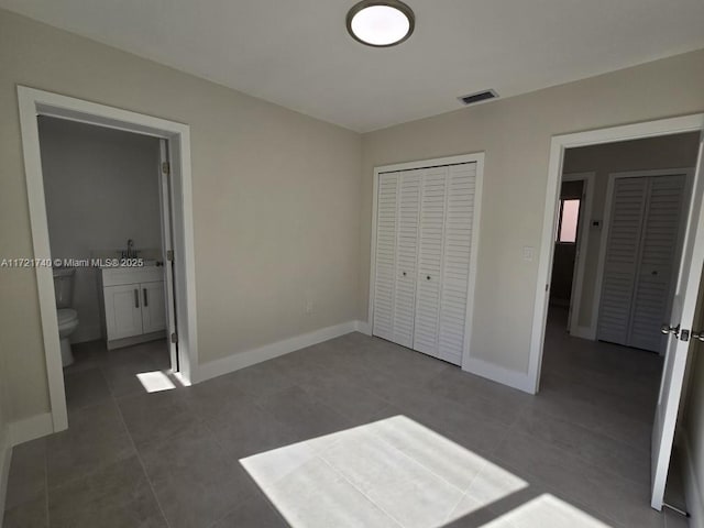 unfurnished bedroom featuring ensuite bath, dark tile patterned floors, and a closet