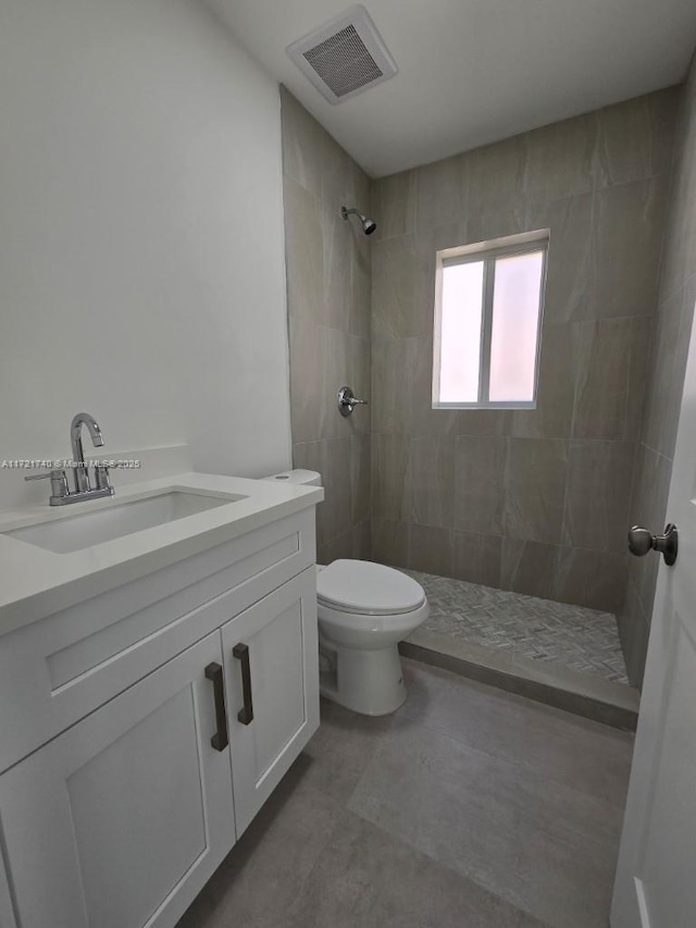 bathroom with tiled shower, vanity, and toilet