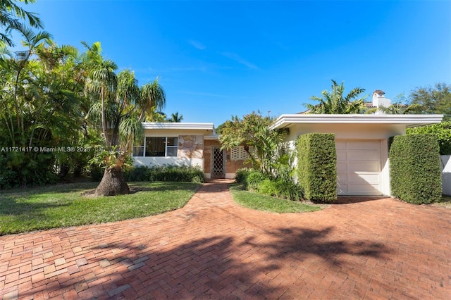 view of front of house with a front yard, decorative driveway, an attached garage, and stucco siding