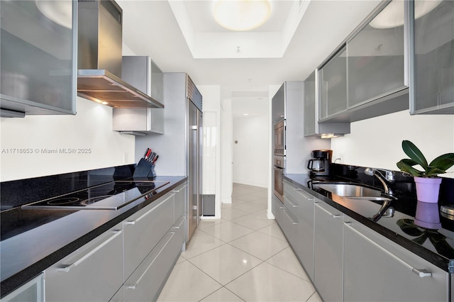 kitchen with a tray ceiling, sink, electric stovetop, wall chimney range hood, and gray cabinets