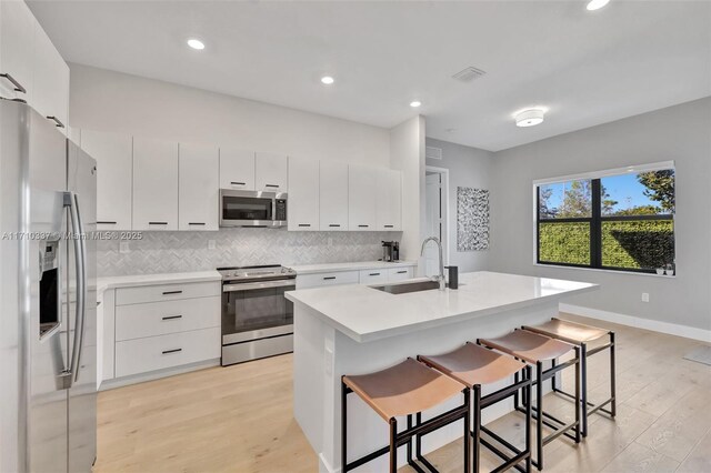 kitchen with a kitchen breakfast bar, sink, an island with sink, white cabinetry, and stainless steel appliances