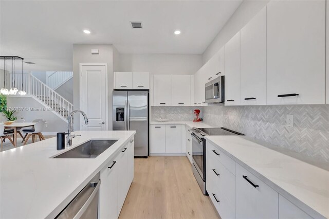 kitchen featuring white cabinetry, sink, hanging light fixtures, and appliances with stainless steel finishes