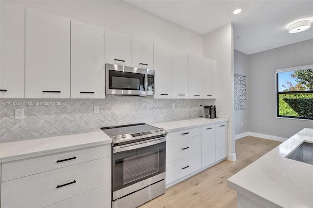 kitchen with white cabinetry, backsplash, appliances with stainless steel finishes, and light hardwood / wood-style flooring