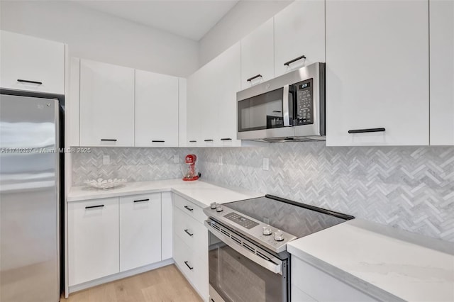 kitchen featuring decorative backsplash, light stone countertops, stainless steel appliances, light hardwood / wood-style floors, and white cabinetry