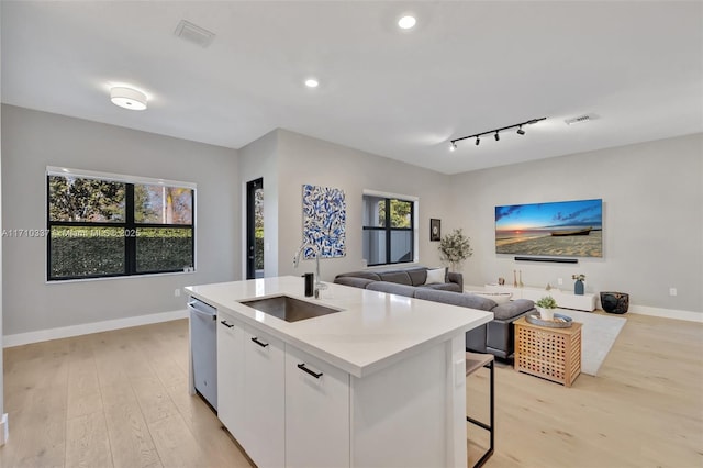 kitchen with sink, stainless steel dishwasher, light hardwood / wood-style floors, a center island with sink, and white cabinets