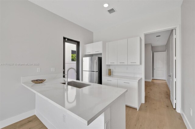 kitchen with stainless steel fridge, kitchen peninsula, sink, and white cabinets