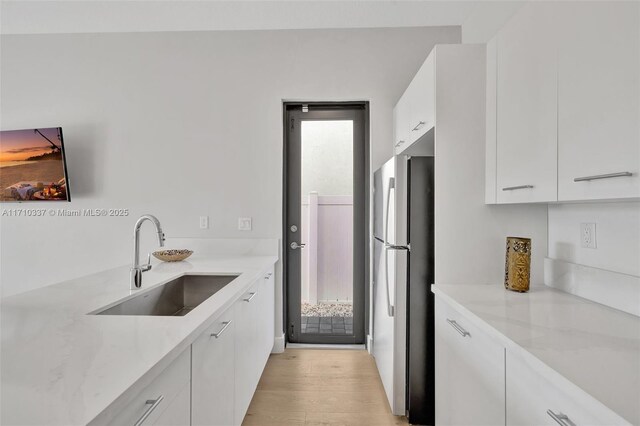 kitchen with sink, light hardwood / wood-style flooring, stainless steel fridge, light stone countertops, and white cabinetry