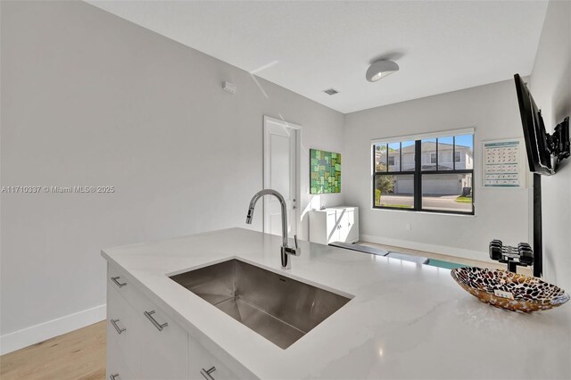 kitchen with white cabinetry, sink, light stone countertops, and light hardwood / wood-style flooring