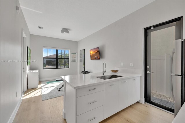 kitchen with kitchen peninsula, sink, light hardwood / wood-style flooring, white cabinets, and white fridge